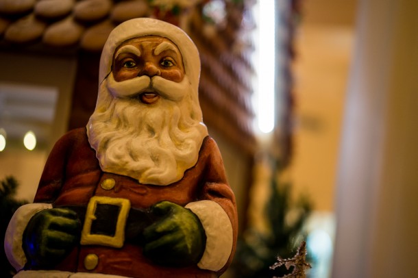 There are many Santa's around the gingerbread house.