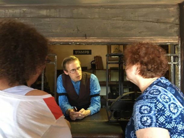 Two women talking to an 1840's themed postmaster through an old post office window