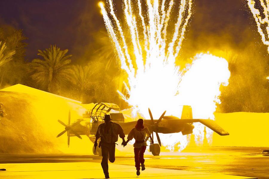 Actors portraying Indiana Jones and Marion run away from an exploding plane